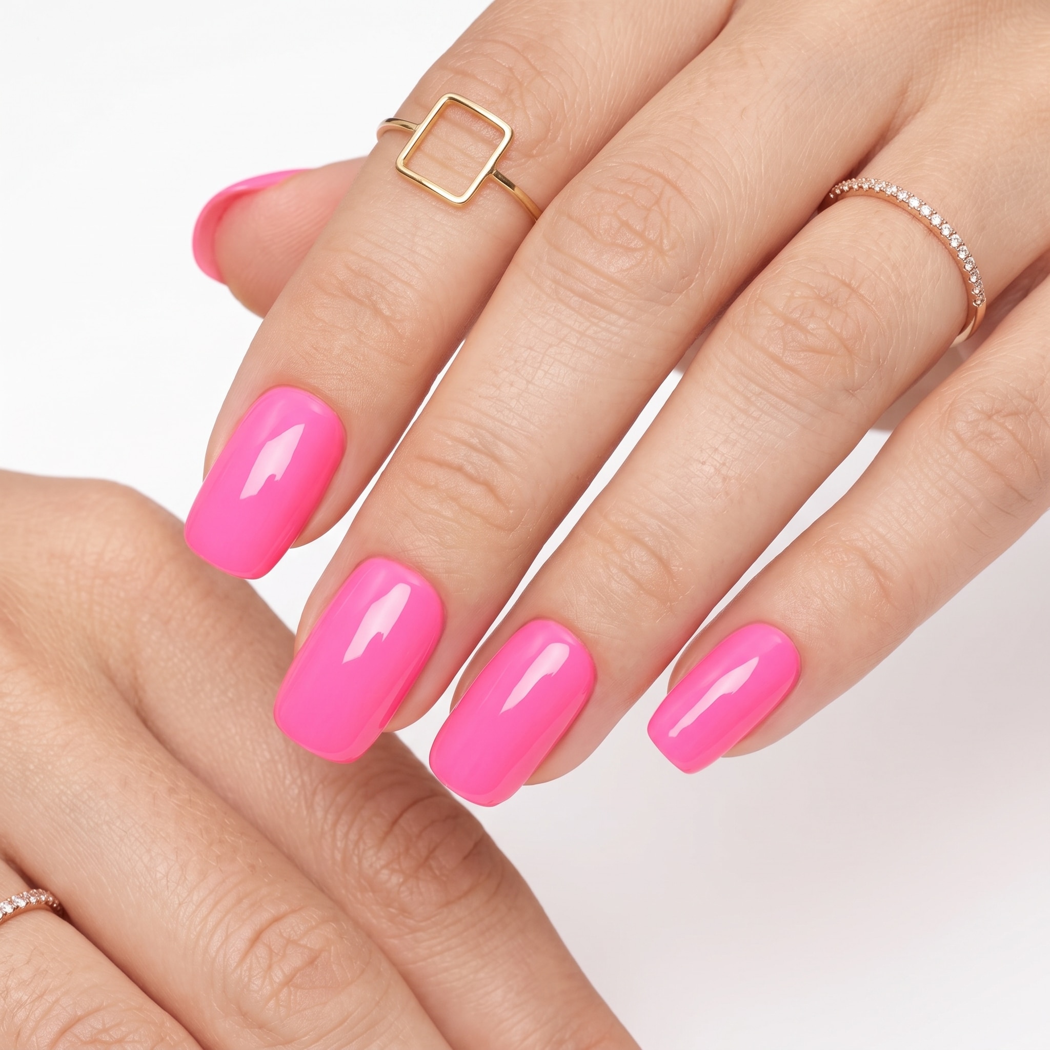 Bright hot pink gel nails on a dark-skinned hand with fine gold rings