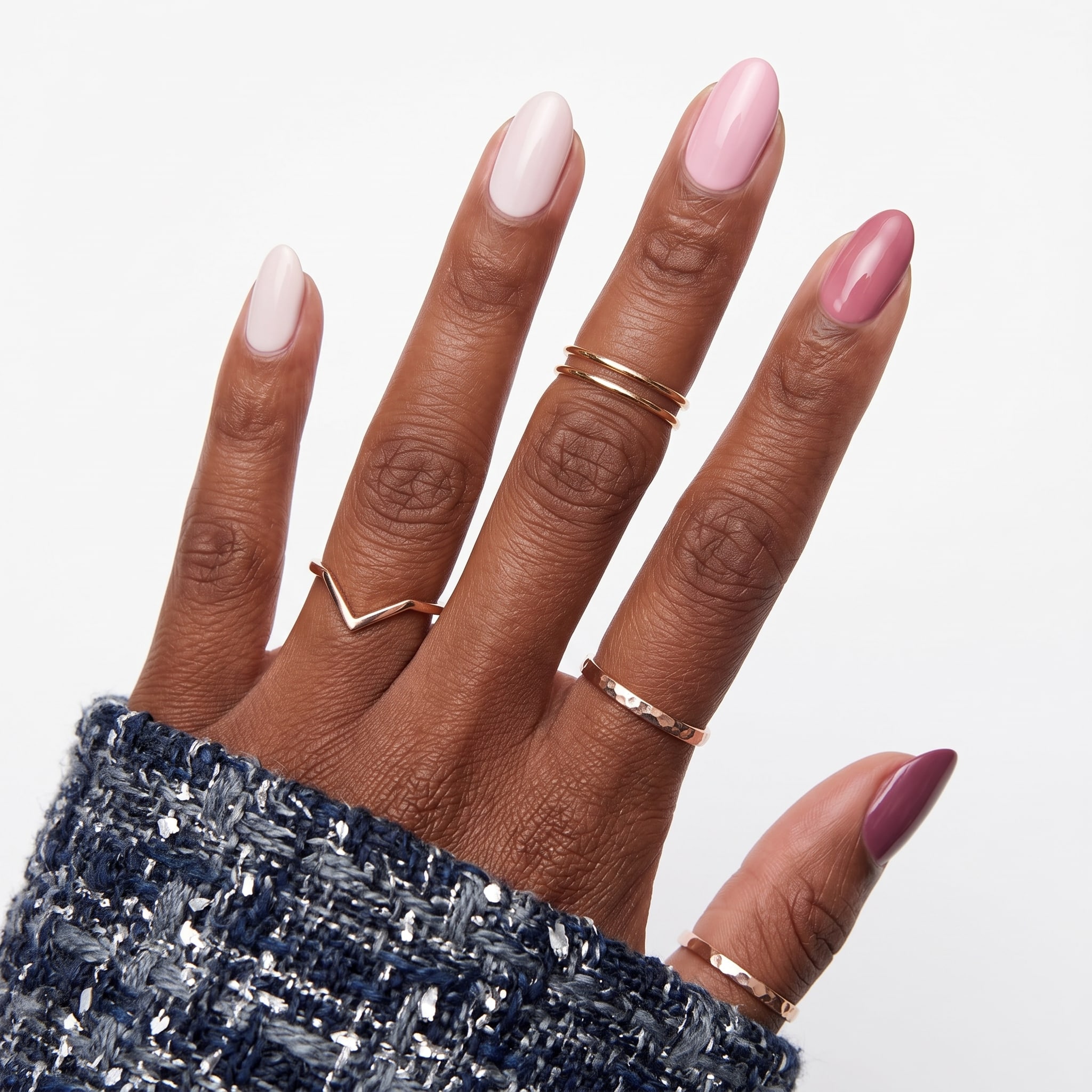 Glossy light pink nails on a hand with delicate gold rings