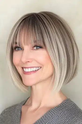 Wispy Bob With Bangs for Fine Hair Haircut on a smiling woman with brownish blonde hair.